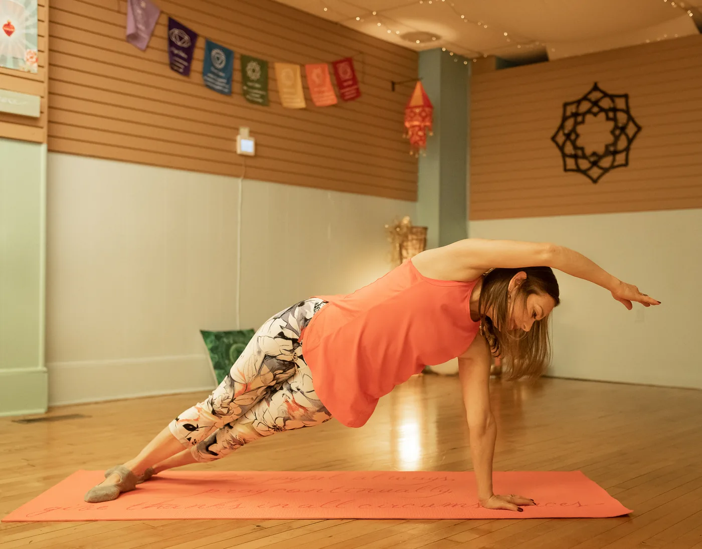 A student practicing side plank on an orange mat in the Grace Yoga and Pilates studio